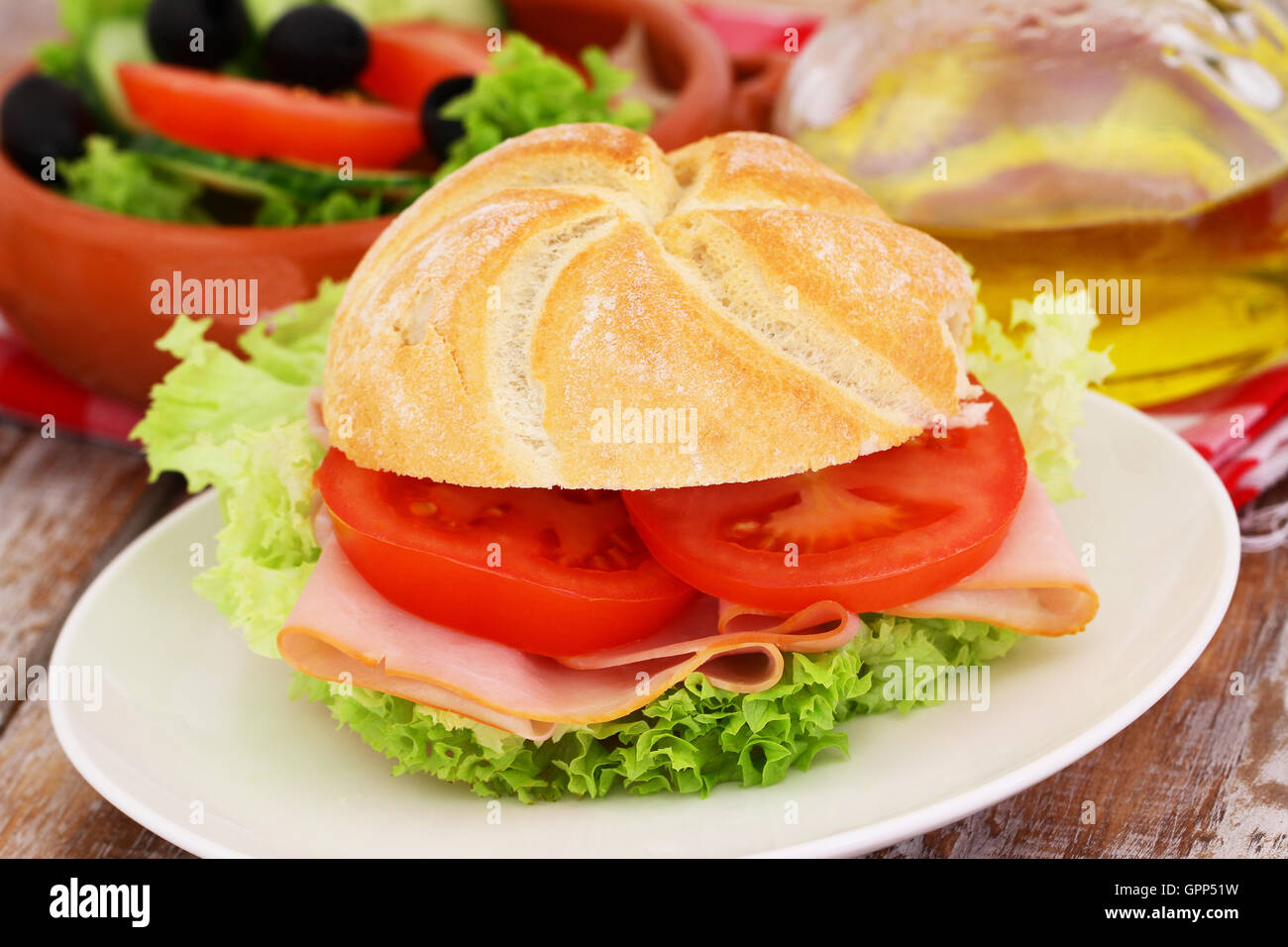 Lunch consisting of bread roll with chicken, tomatoes and lettuce and bowl of salad Stock Photo