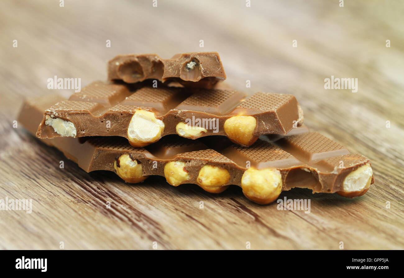 Pieces of milk chocolate with whole hazelnuts stacked up on wooden