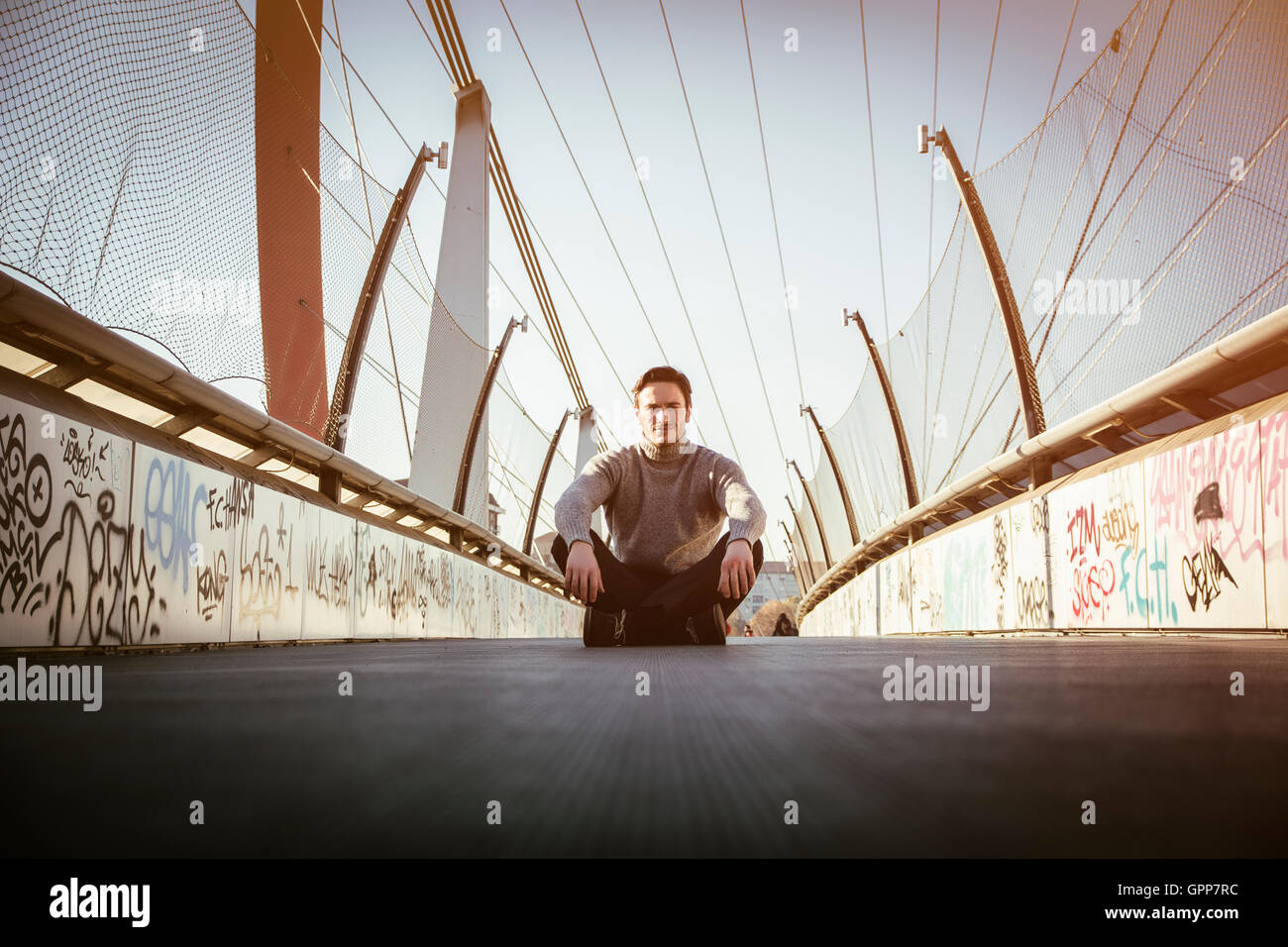Handsome young man sitting outdoors in urban environment looking at camera, wearing winter clothes Stock Photo