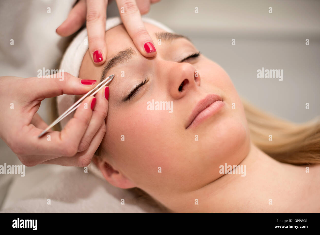 Plucking eyebrows with tweezer by beautician in beauty salon. Stock Photo