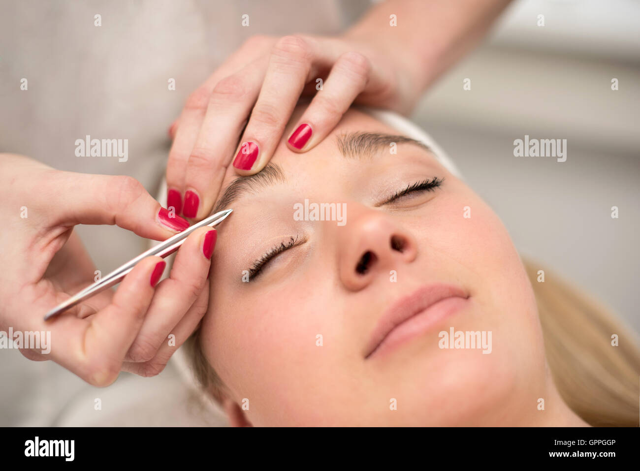Plucking eyebrows with tweezer by beautician in beauty salon. Stock Photo