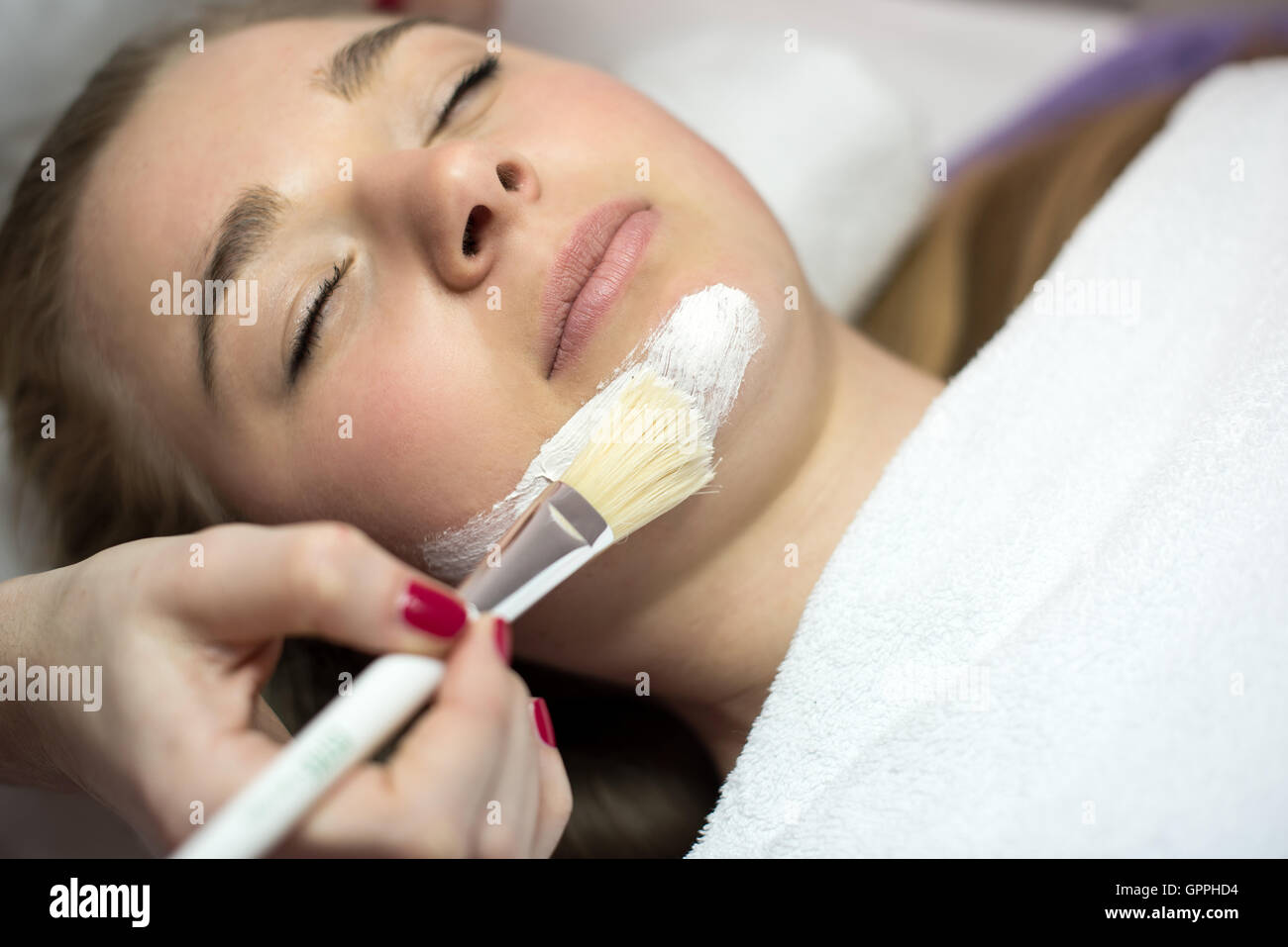 Portrait of young woman while having facial mask apply by beautician. Stock Photo