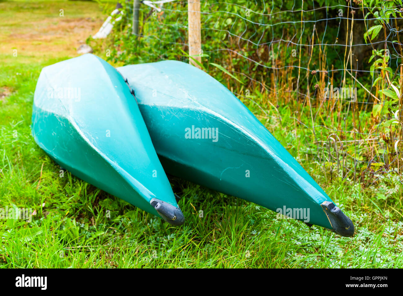 Two upside down plastic canoes or kayaks on dry land. The canoes are