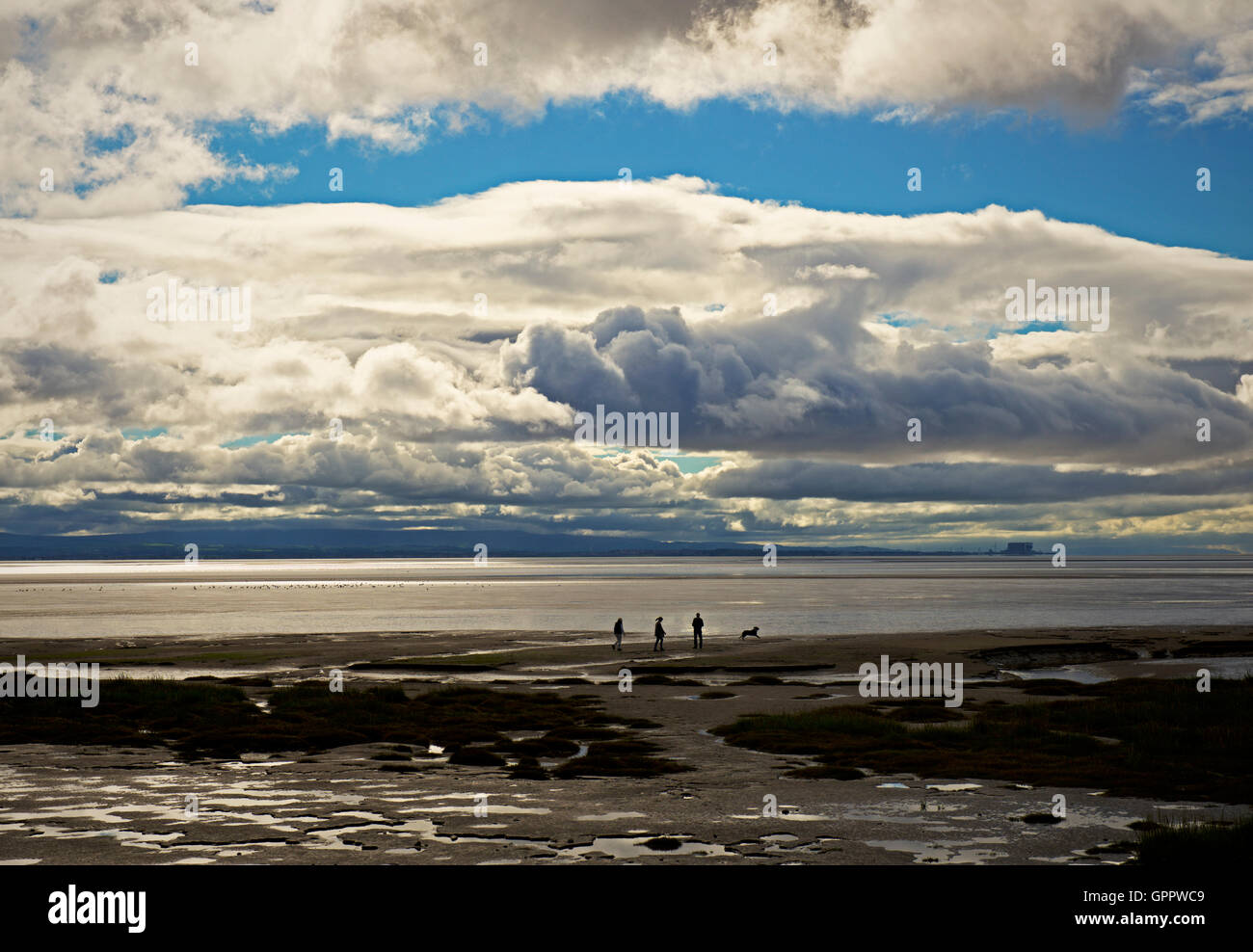 People and dog walking on the mudflats of Morecame Bay, near