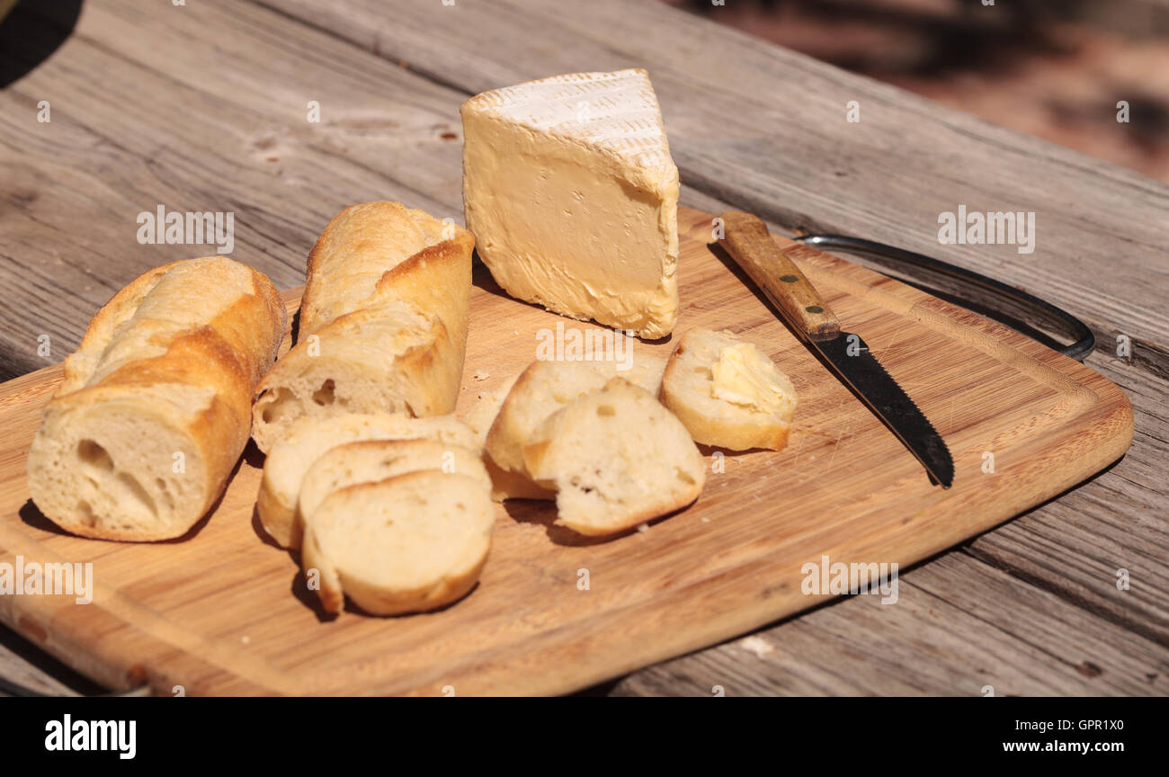 French bread and triple cream brie cheese on a cutting board with a knife. Stock Photo