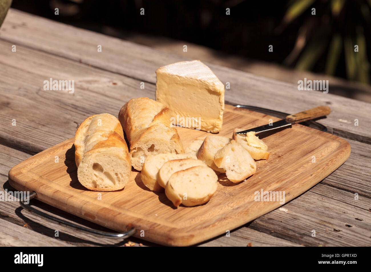 French bread and triple cream brie cheese on a cutting board with a knife. Stock Photo