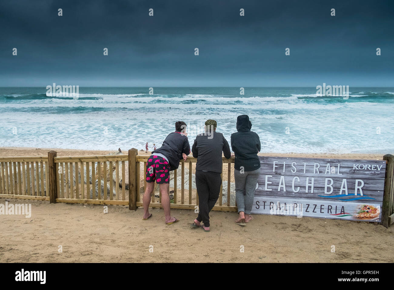 Three holidaymakers stand overlooking Fistral Beach as rain approaches. Stock Photo