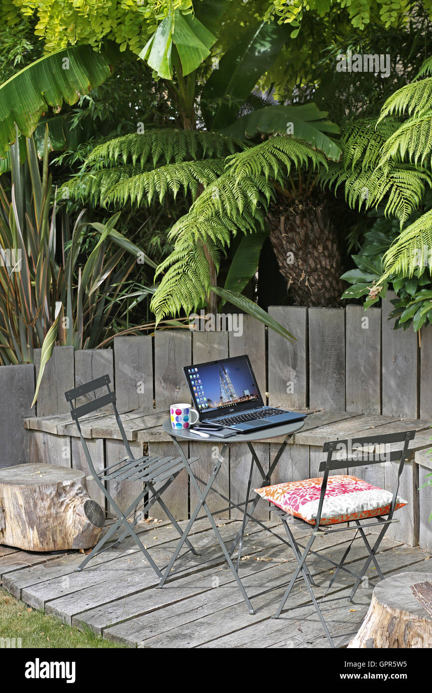 Working from home: a laptop computer, smart phone and coffee mug on a garden table in an urban, UK garden on a summer day. Stock Photo