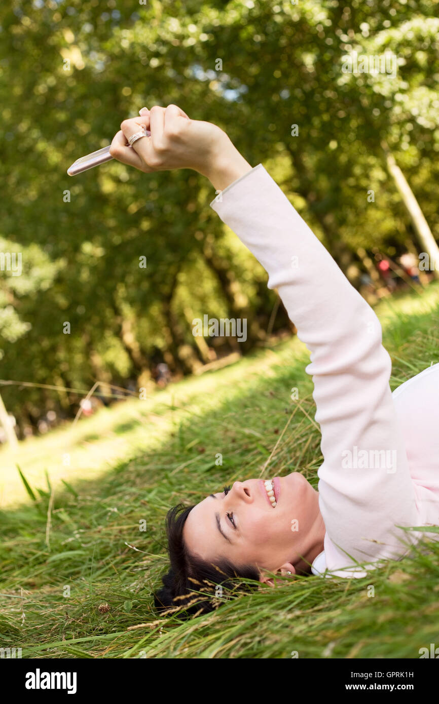 young woman lying on the grass taking a selfie Stock Photo