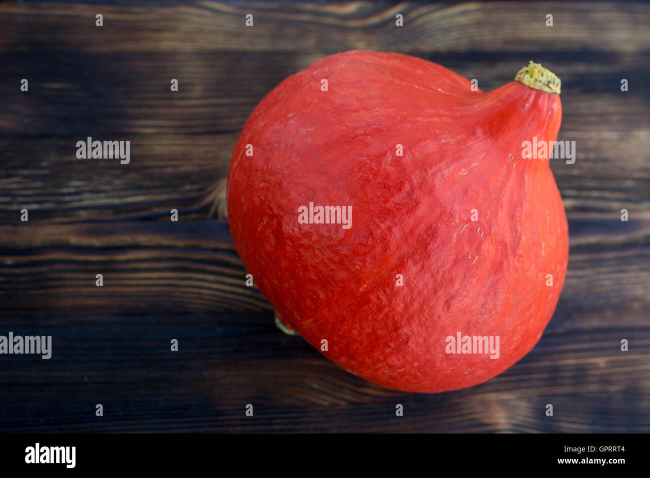Red orange pumkin with hard rind laying diagonally on dark brown wooden ...