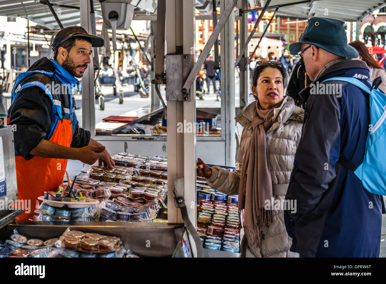 A fish salesman in a street market is selling his products. His customers is an adult couple, almost ready to decide what they s Stock Photo