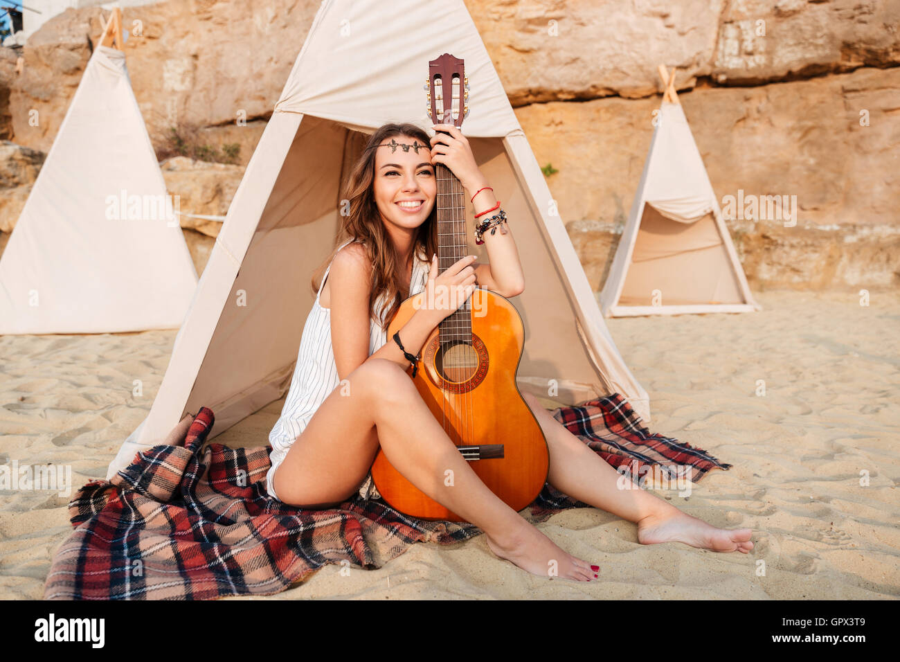 Smiling young hippie woman posing with guitar at the beach tent Stock Photo