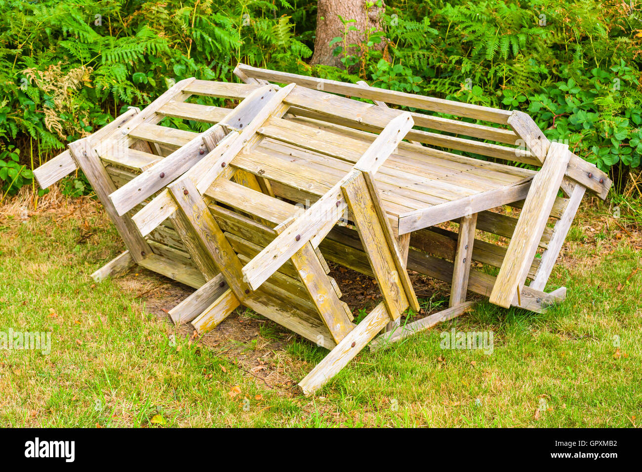 Set of unpainted wooden outdoor furniture on a patch of grass with forest undergrowth in the background. Stock Photo