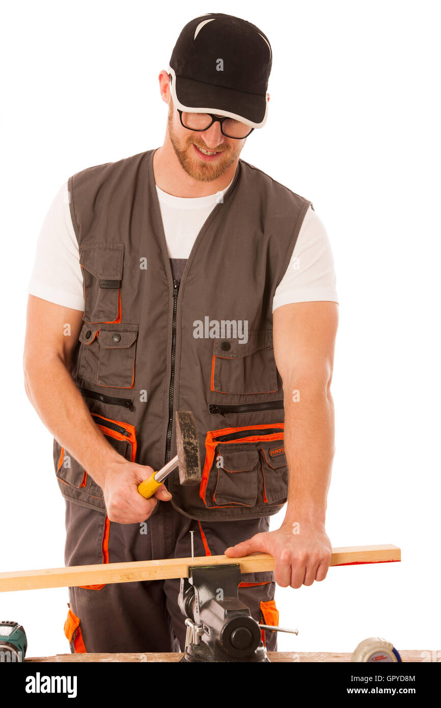 Handyman in work clothing hammering nail with hammer in home workshop isolated over white. Stock Photo