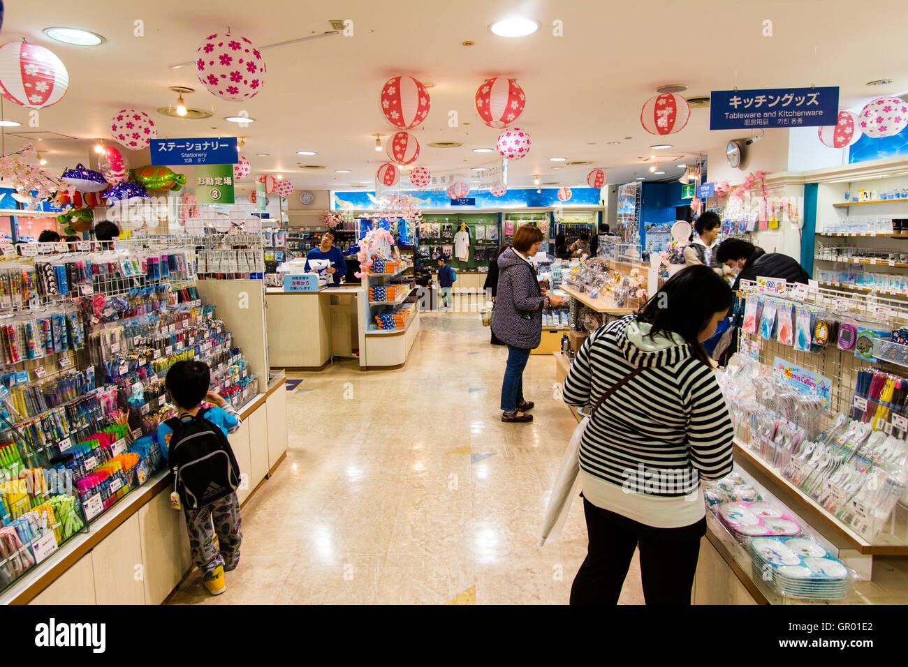 Interior of the gift shop at the Osaka Aquarium, Kaiyukan. View along two display stands with various souvenirs and Japanese women and a child looking. Stock Photo