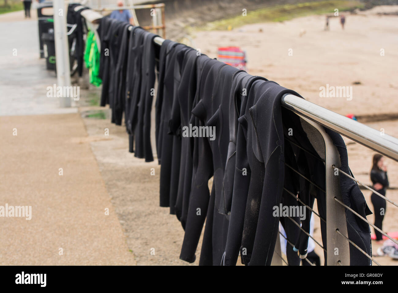 Photo shows a row of wetsuits hung over the railings at West Strand, Portrush, Northern  Ireland between Surf School Classes. Stock Photo