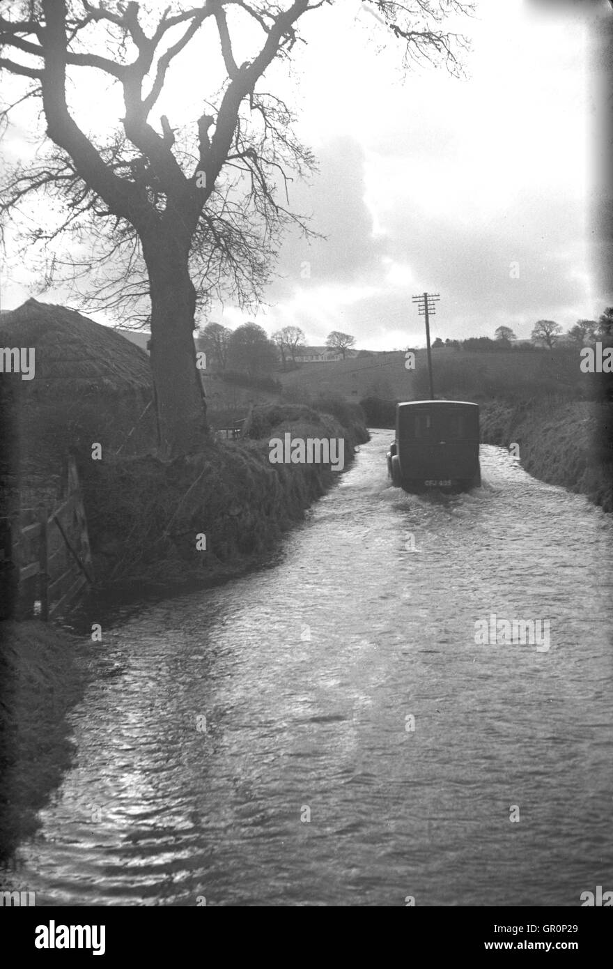 1938, historical, small delivery van makes it's way through the water on a flooded country lane near Chagford, Devon, England, which is on the edge of the Dartmoor National park and is close to the River Teign. Stock Photo