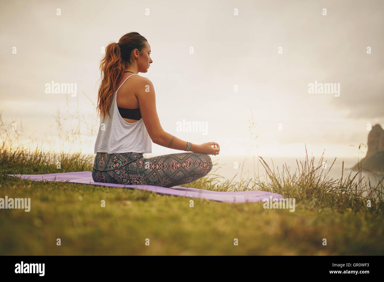 Rear view of young woman doing yoga meditation outdoors. fitness female model practicing yoga. Stock Photo