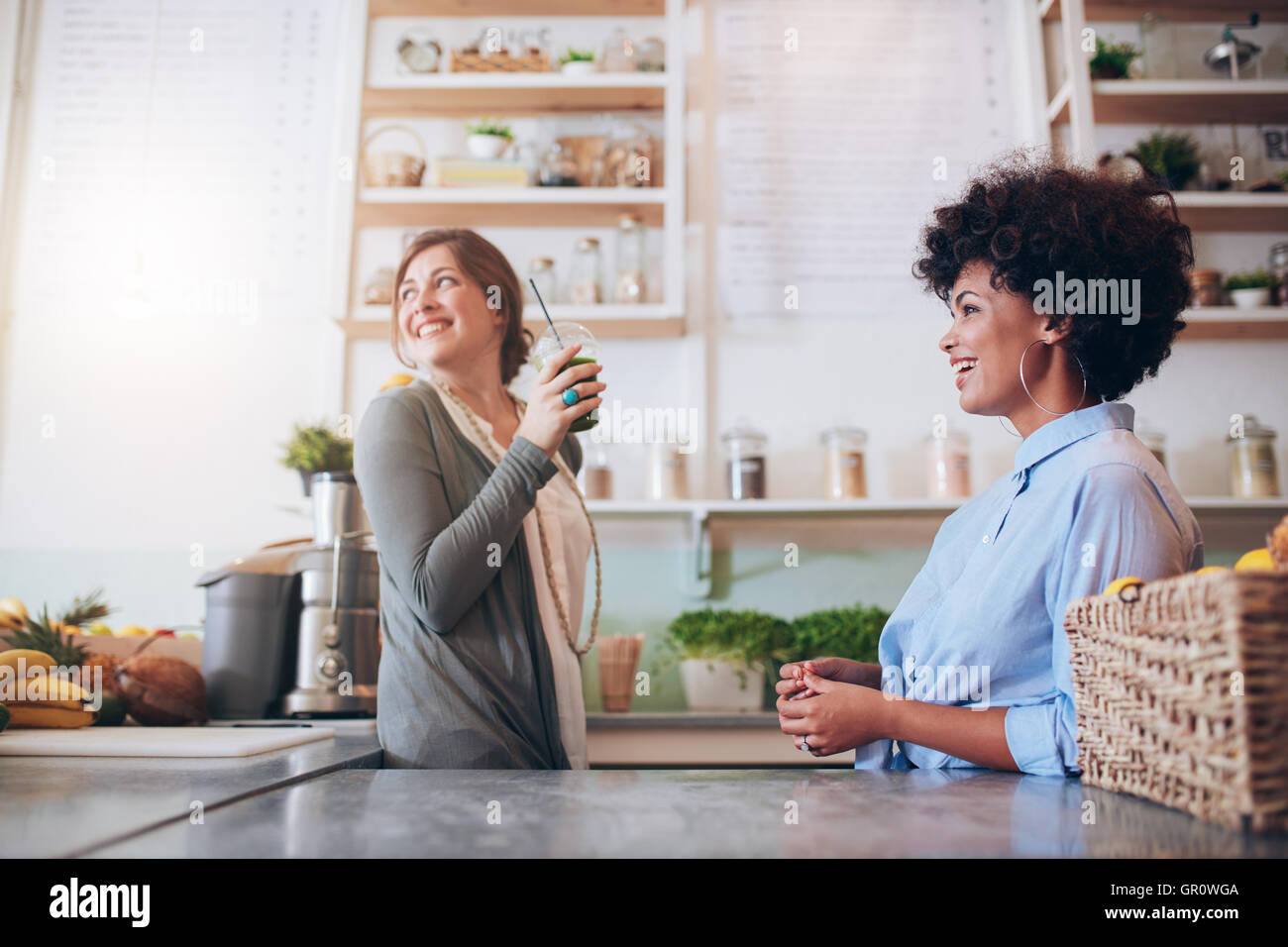 Two young female juice bar employees standing behind counter. Young women working at fruit juice bar. Stock Photo