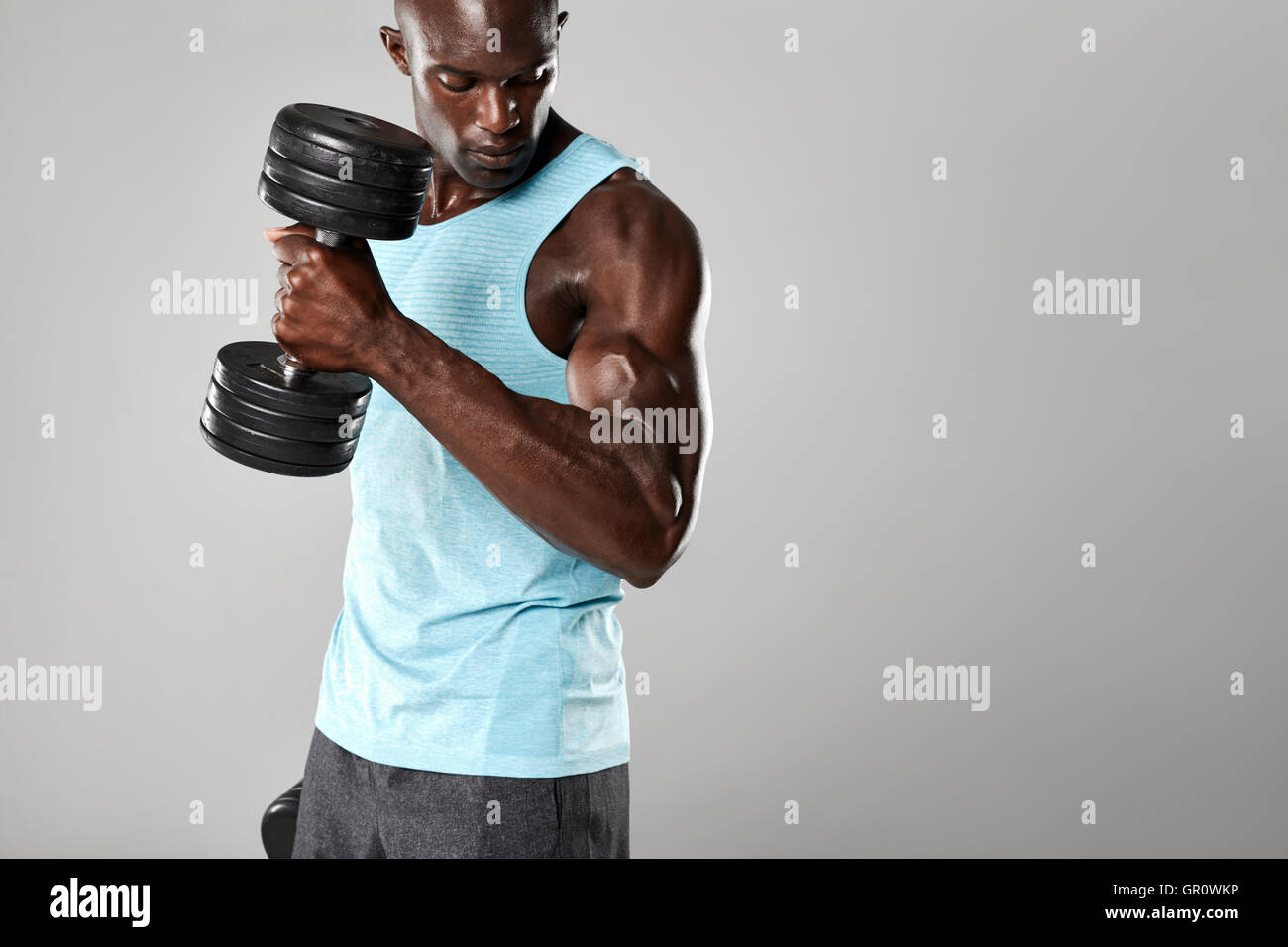 Shot of fit and young man working out with dumbbells on grey background. Muscular man doing weight exercise. Stock Photo