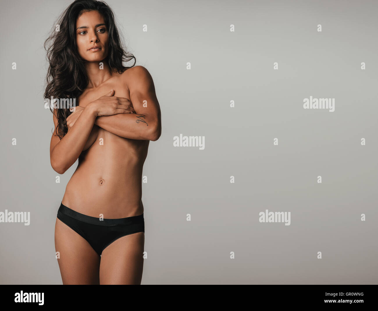Single beautiful woman in black underwear covering breasts over gray background with copy space Stock Photo