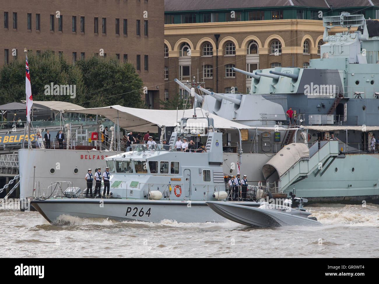 The Maritime Autonomy Surface Testbed (MAST), an unmanned surface vessel (right) and its escort HMS Archer (left) pass HMS Belfast as the MAST is tested on the River Thames, London, as part of preparations for the Royal Navy's 'Unmanned Warrior' test program this autumn. Stock Photo