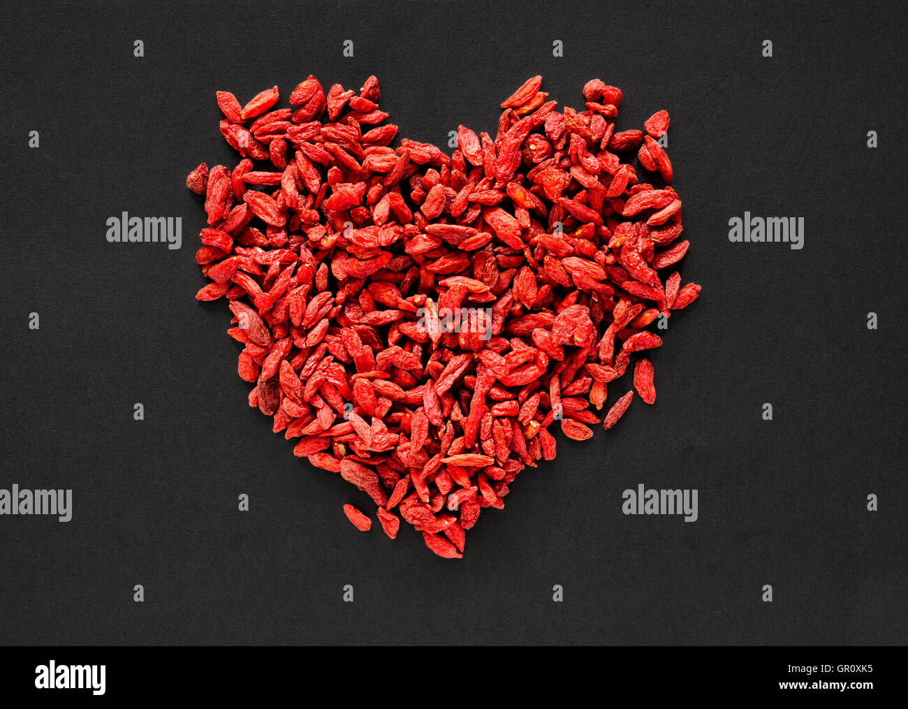 Raw dried goji berries arranged in a heart shape on a black background Stock Photo