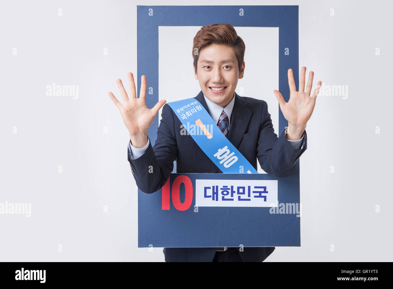 Portrait of young smiling candidate in suit waving hands on poster Stock Photo