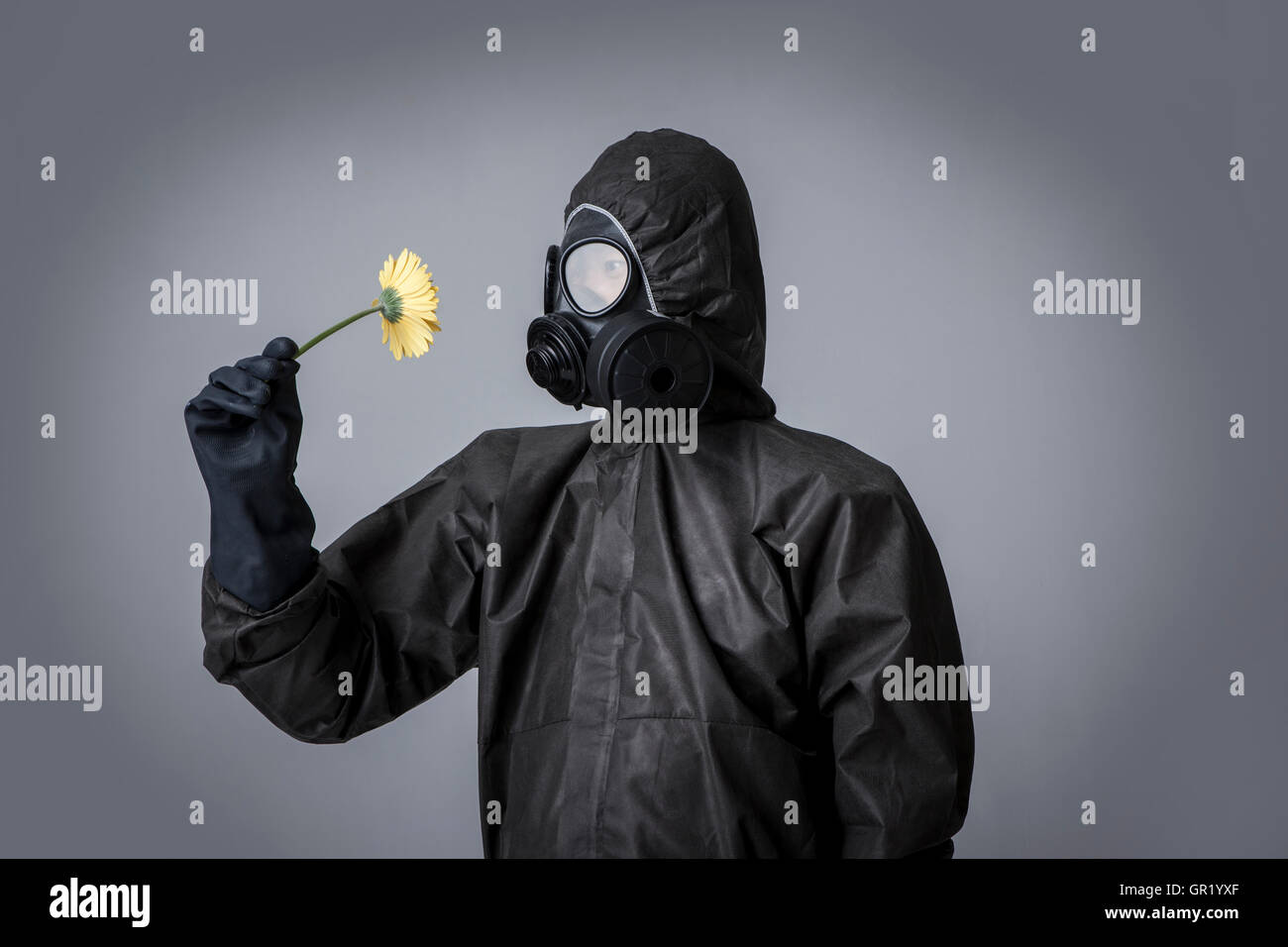 Young man wearing gas mask and black clothes smelling flower Stock Photo