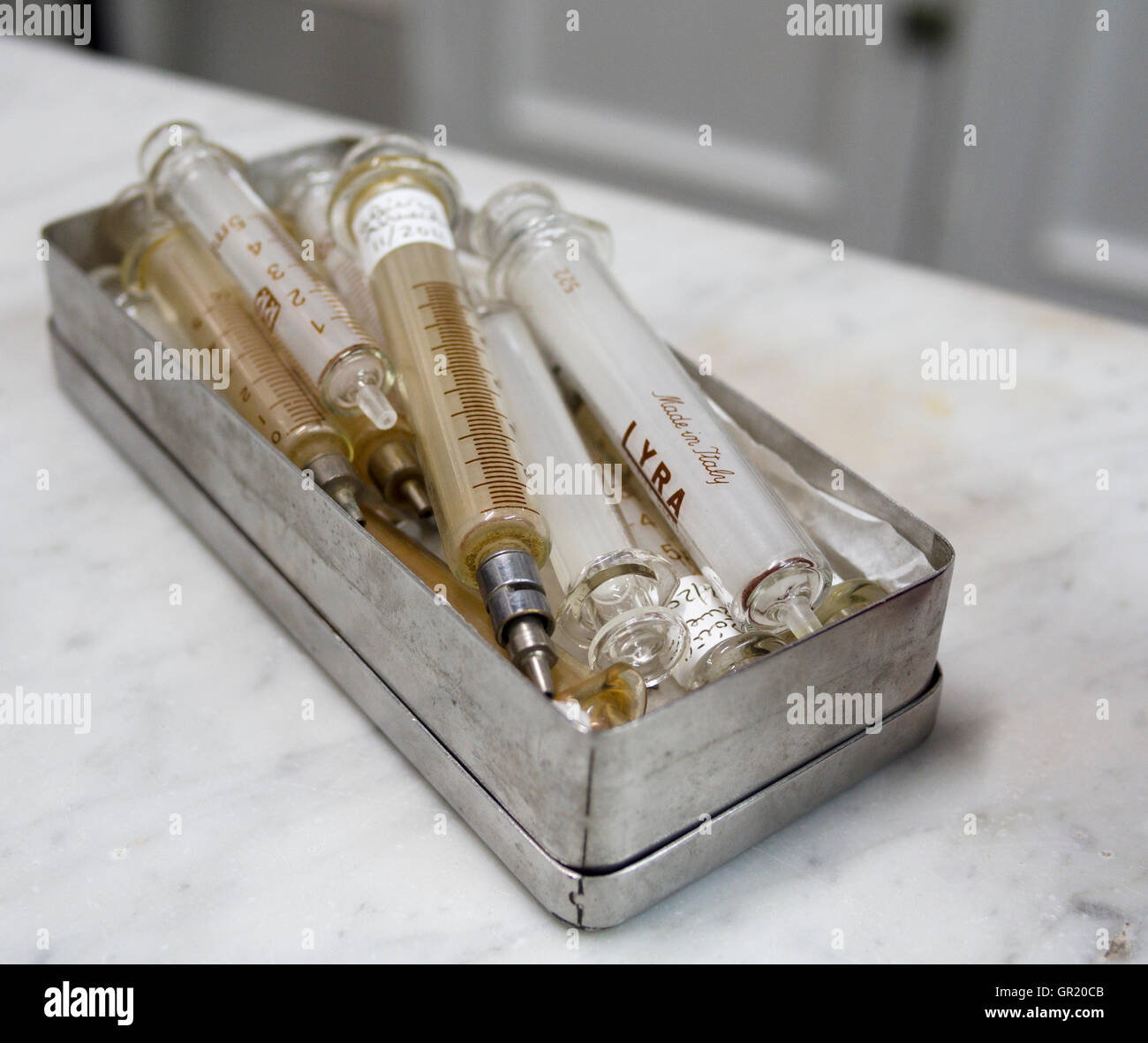 A box of old glass syringes. A metal box containing many glass syringes in an old pharmacy. One is labeled Lyra, made in italy. Stock Photo