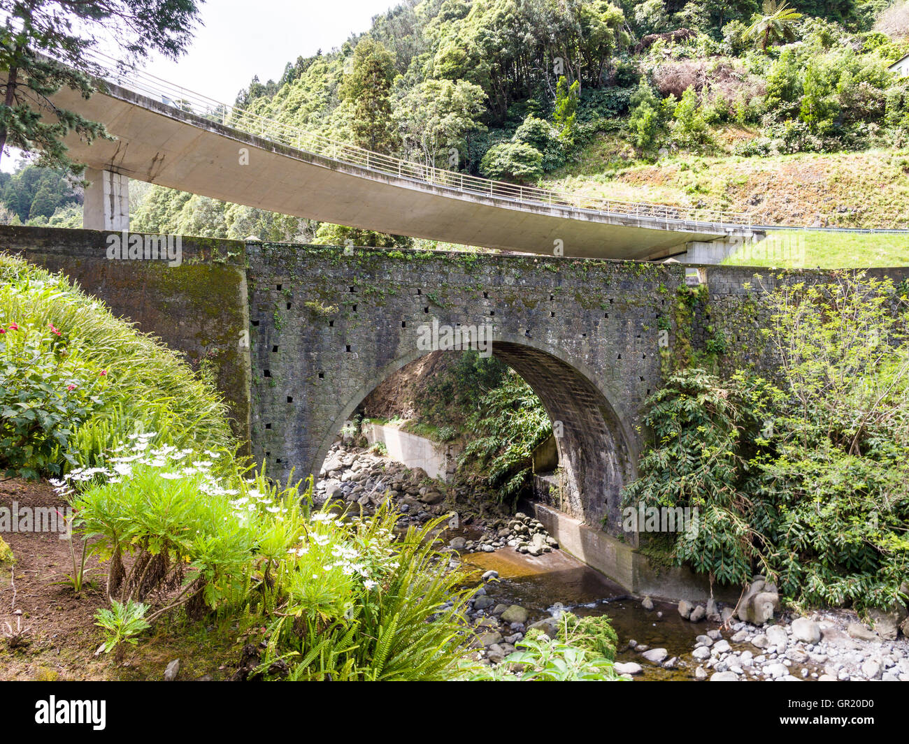 Old and New Bridges. An old stone arched bridge over a stream with a new highway fly-over bridge above. Stock Photo