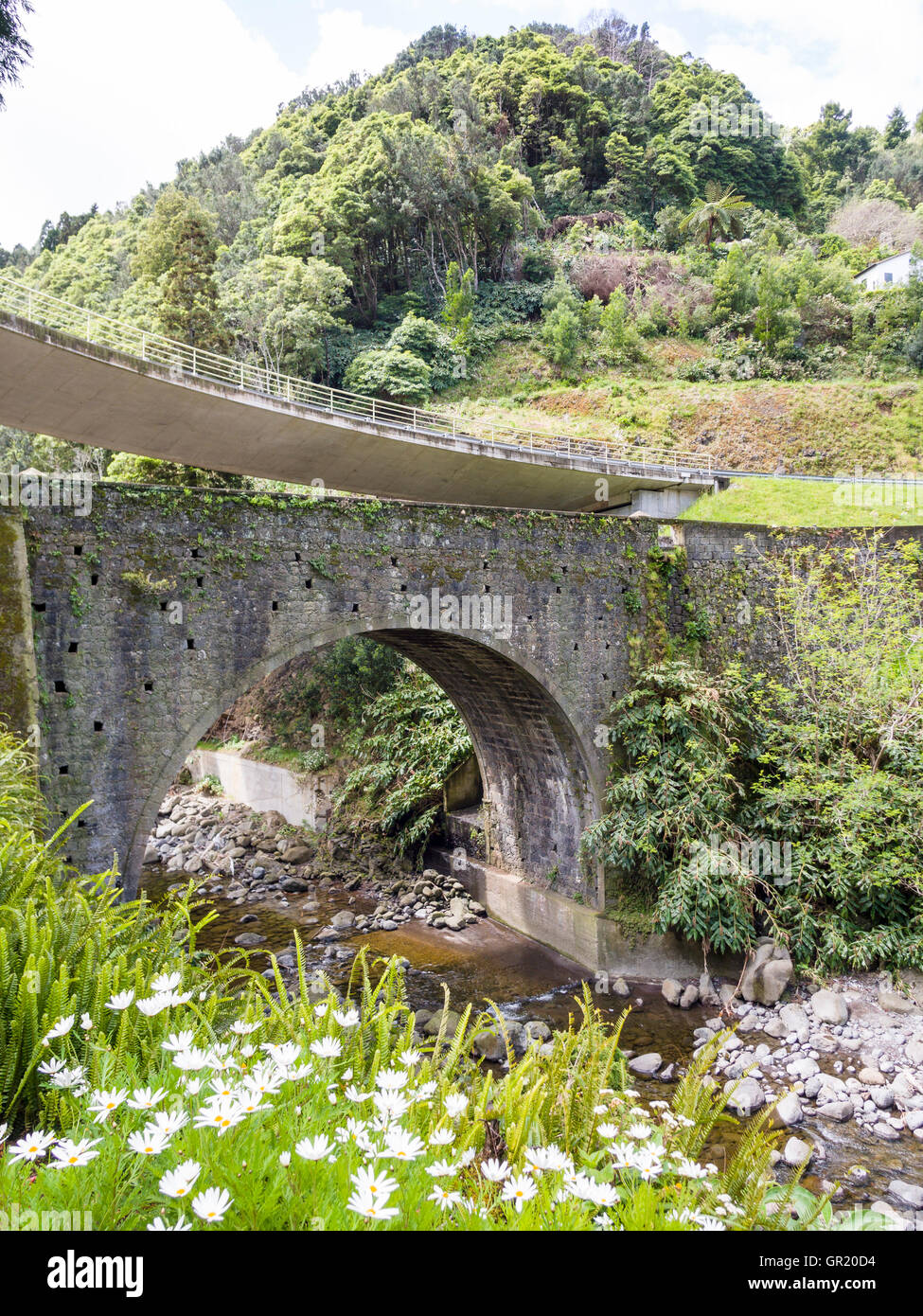 Old and New Bridges. An old stone arched bridge over a stream with a new highway fly-over bridge above. Stock Photo