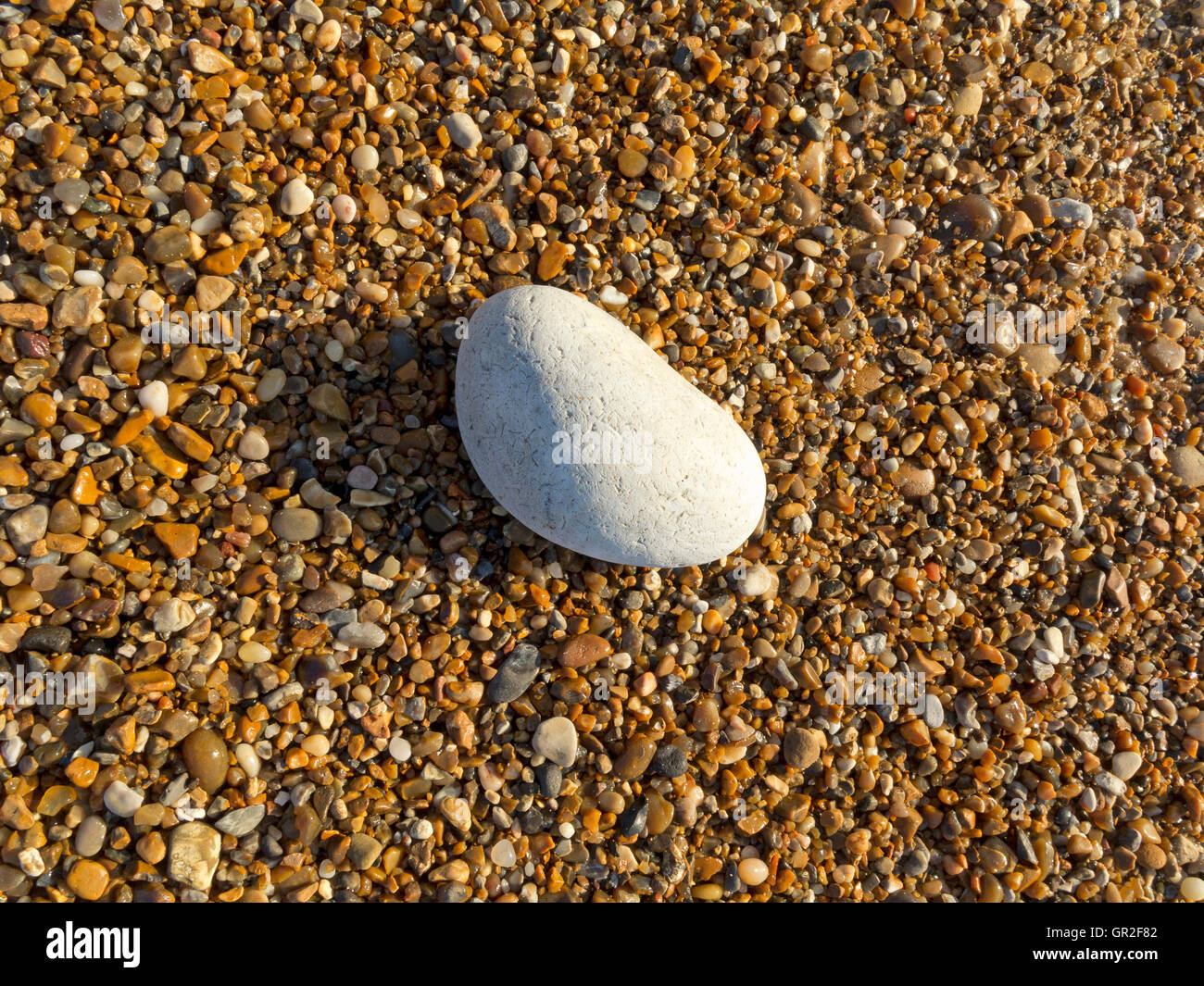 A flat overhead shot of small beach pebbles with a single large white pebble Stock Photo