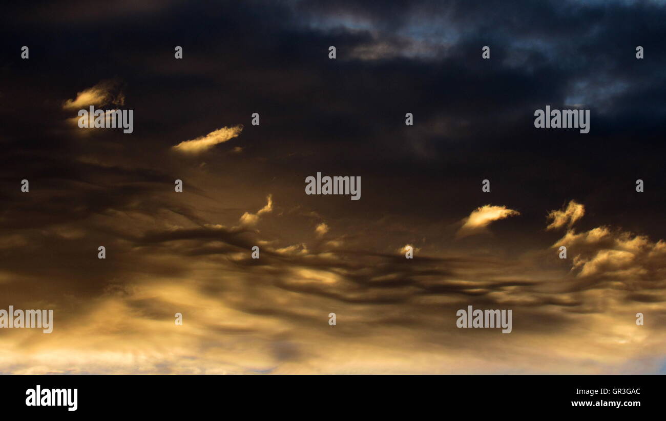 Gorgeous gold and dark whispy clouds during stormy sunset Stock Photo