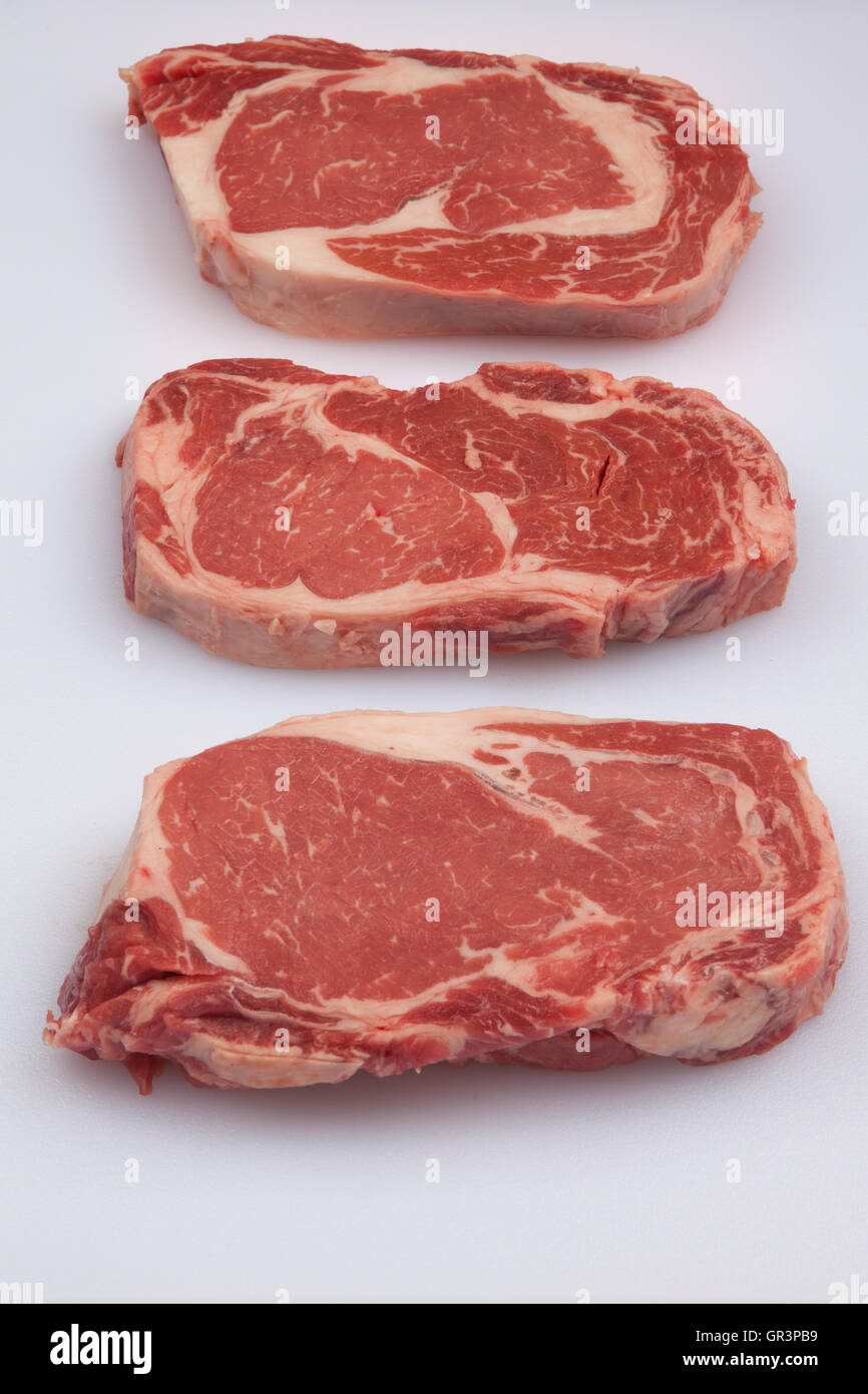 Three Rib Eye Steaks, white chopping board, brown background meat, protein, beef, dinner,steaks, marble, thick, isolated, Stock Photo