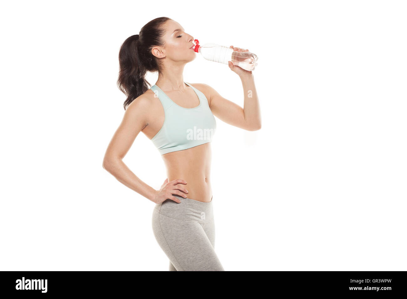 Sporty girl drinking water from a bottle after a workout, fitness training, isolated on white background Stock Photo
