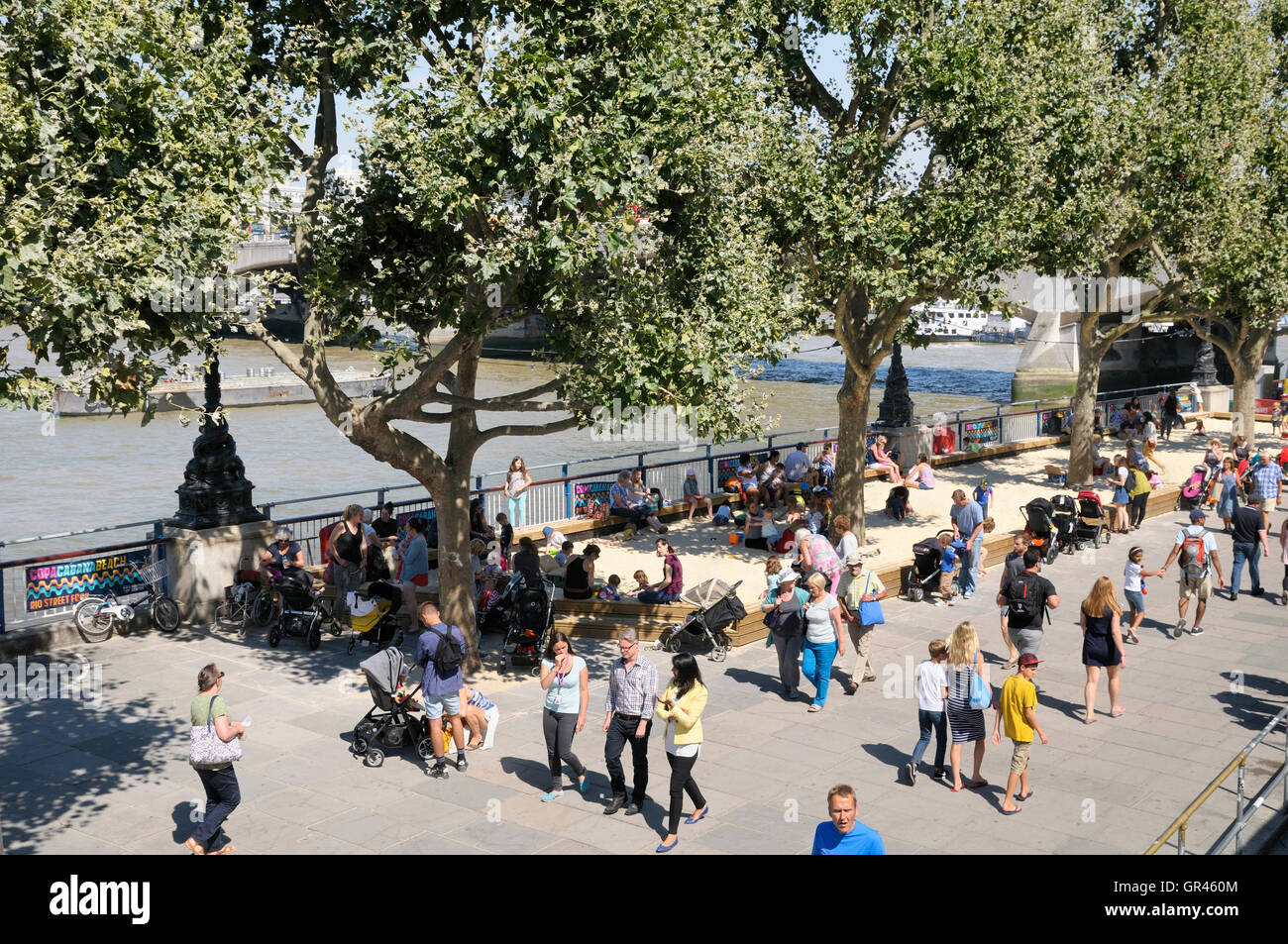 London's South Bank in summer.  People strolling along the Thames Path next to the temporary beaches set up by the River Thames. Stock Photo