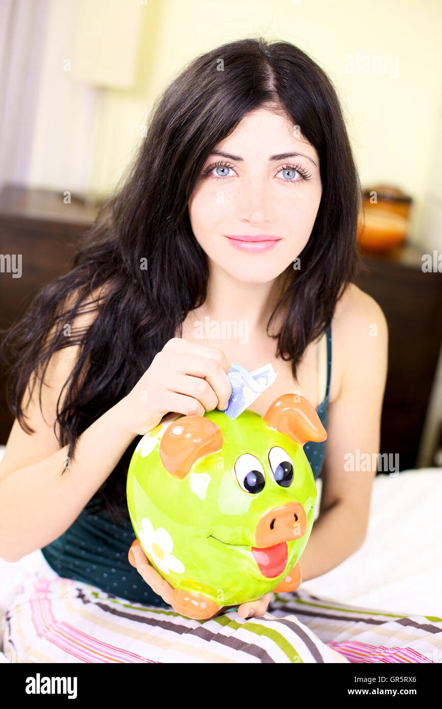 Happy woman putting money in piggy bank Stock Photo - Alamy