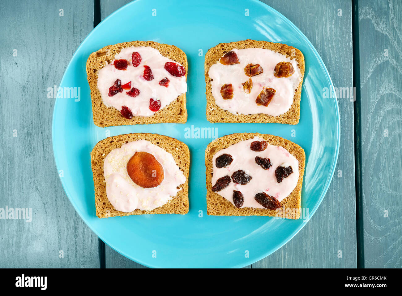 Bread with strawberry cream cheese and dry fruits on blue plate, healthy breakfast setting from above. Stock Photo