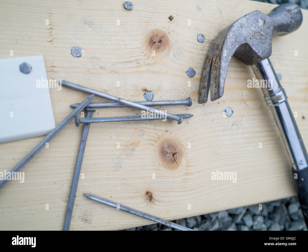 A hammer and nails lying on a wooden plank. Some nails are hammered in to the plank. Stock Photo