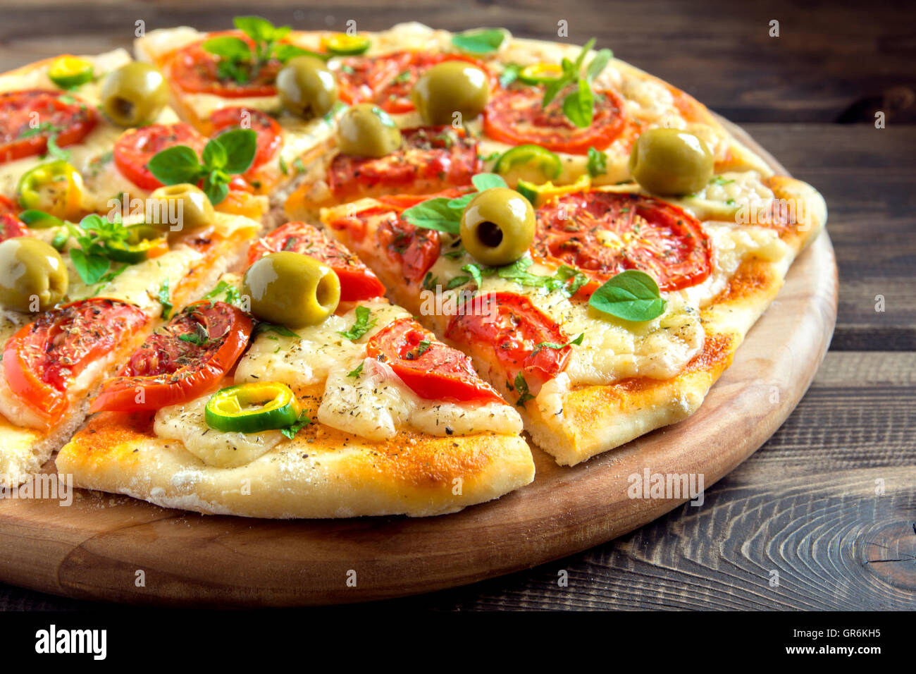 Homemade vegetable pizza with tomatoes, green olives, pepper, basil, oregano and cheese on