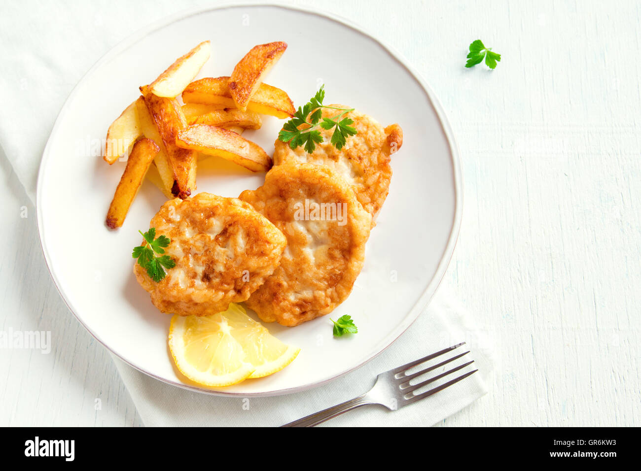 Homemade fish cakes with french fries over white wooden background with