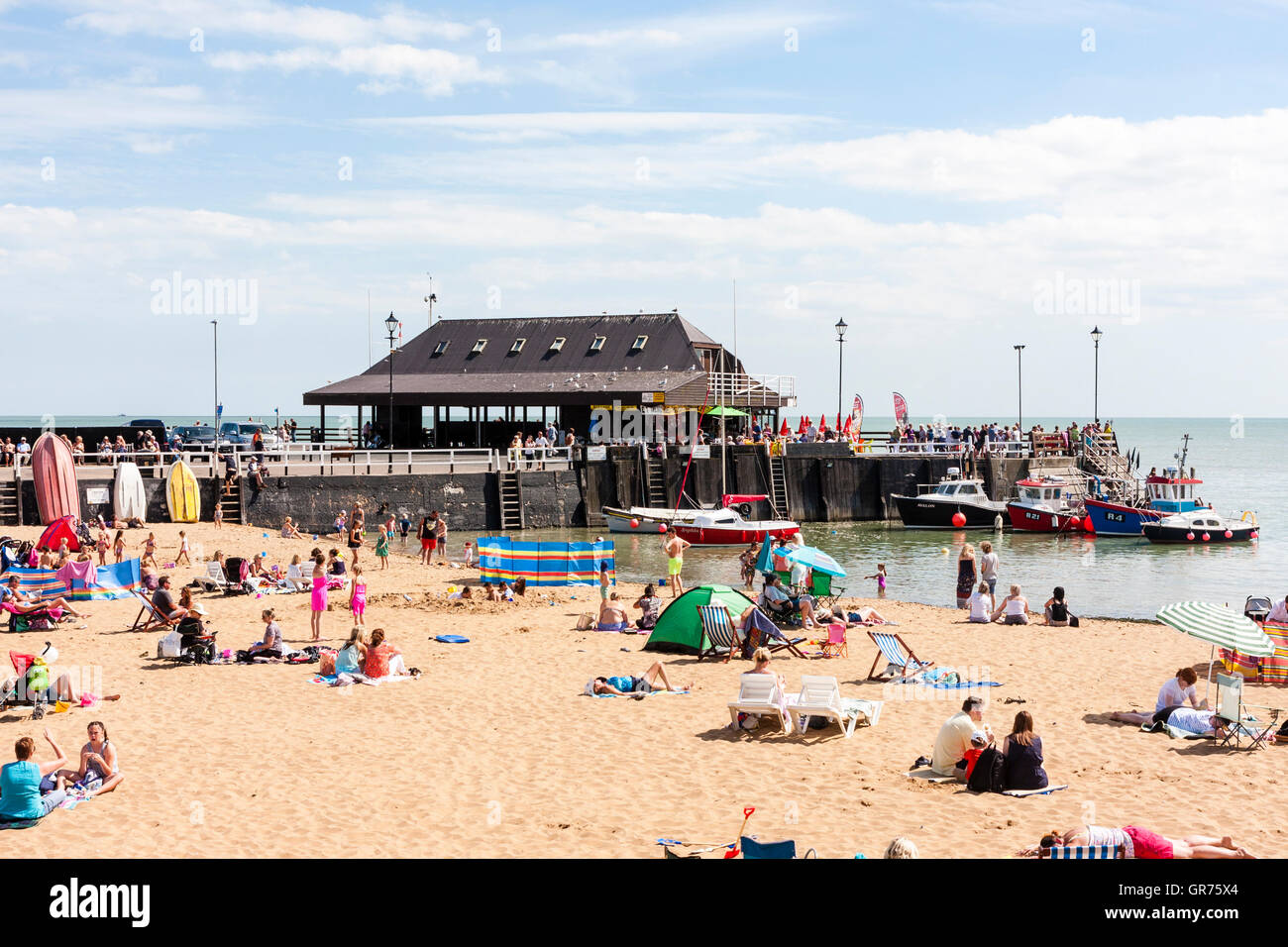 Broadstairs resort town in UK, the main beach with small harbour at one end. Hot summer day with lots of people and families on beach sunbathing. Stock Photo