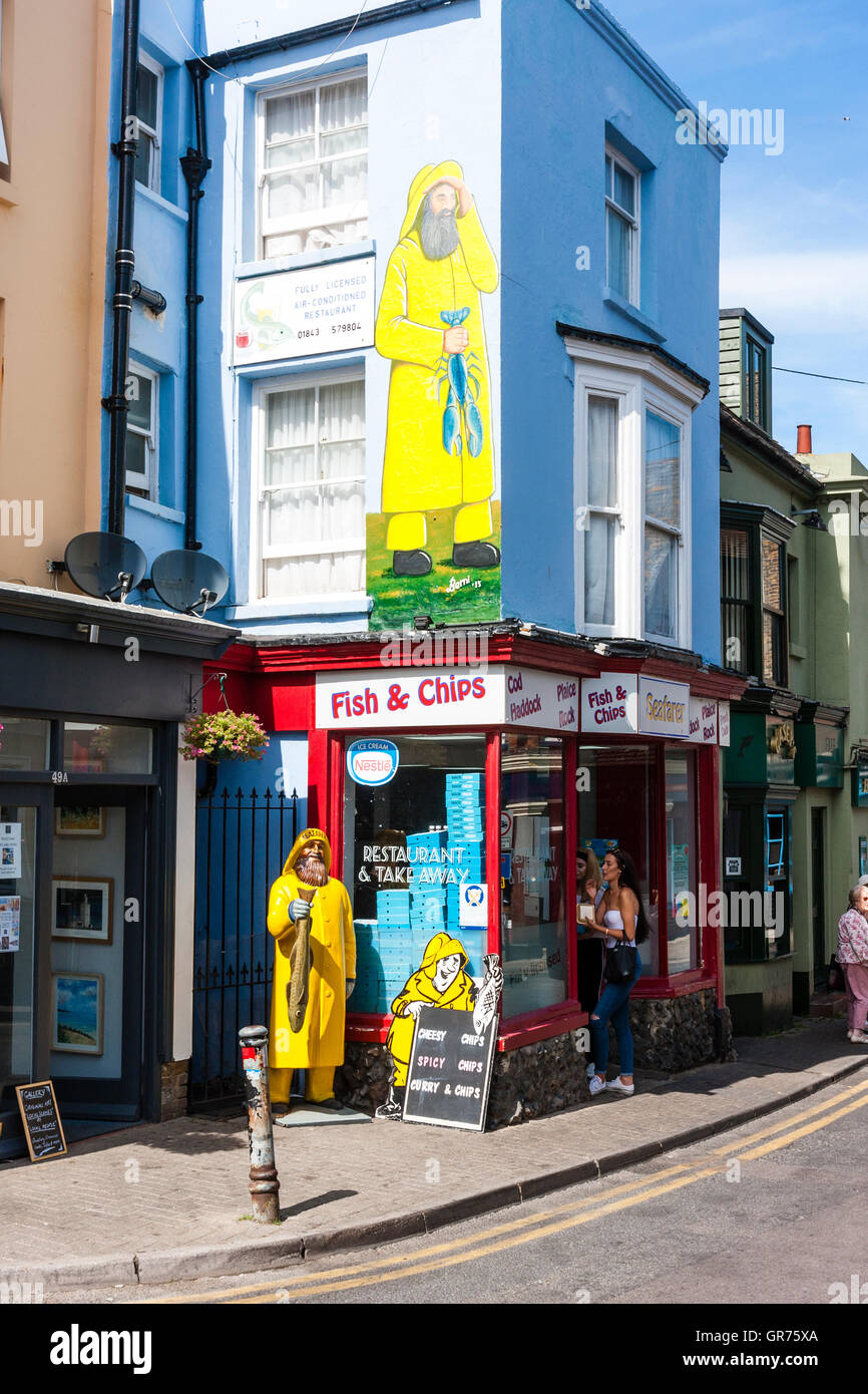 Traditional English fish and chip shop in main street, Broadstairs, UK. Daytime, two teenage women in doorway. Model of fisherman outside. Stock Photo