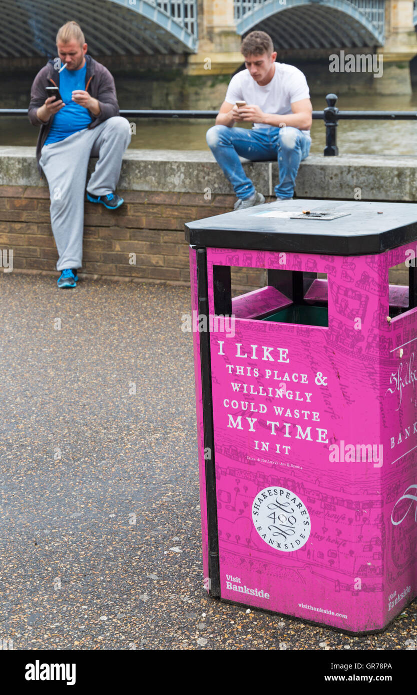 I like this place and willingly could waste my time in it sign on bin with 2 men sat using phones and smoking, Bankside, London Stock Photo