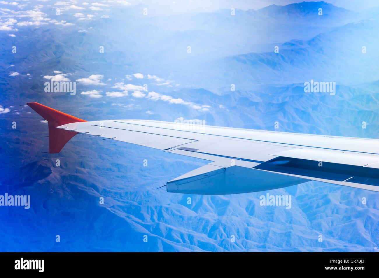 Wing of airplane flying above clouds and Caucasus mountains. View of sky from aircraft, long distance travel by airtransport Stock Photo