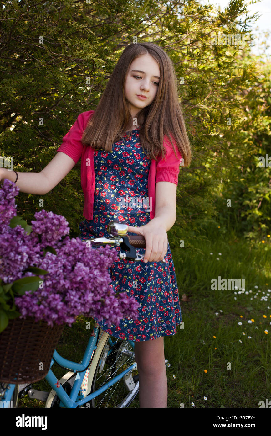 Beautiful teenage girl sitting on a bicycle with a basket of purple ...
