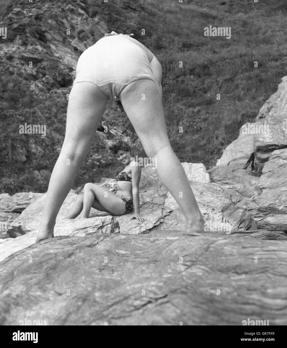 c1950s An amusing and candid portrait of a woman on a beach framed by another's legs. A typical example of perhaps how not to imaginatively frame a photograph of a bathing beauty by using the legs and bottom of another!  Photograph by Tony Henshaw Stock Photo