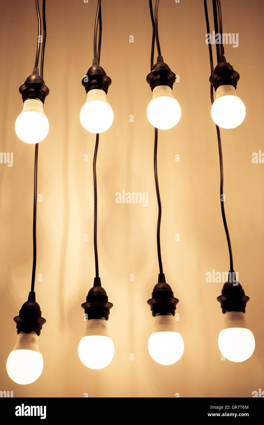 Lit lightbulbs hanging on wires against wall Stock Photo