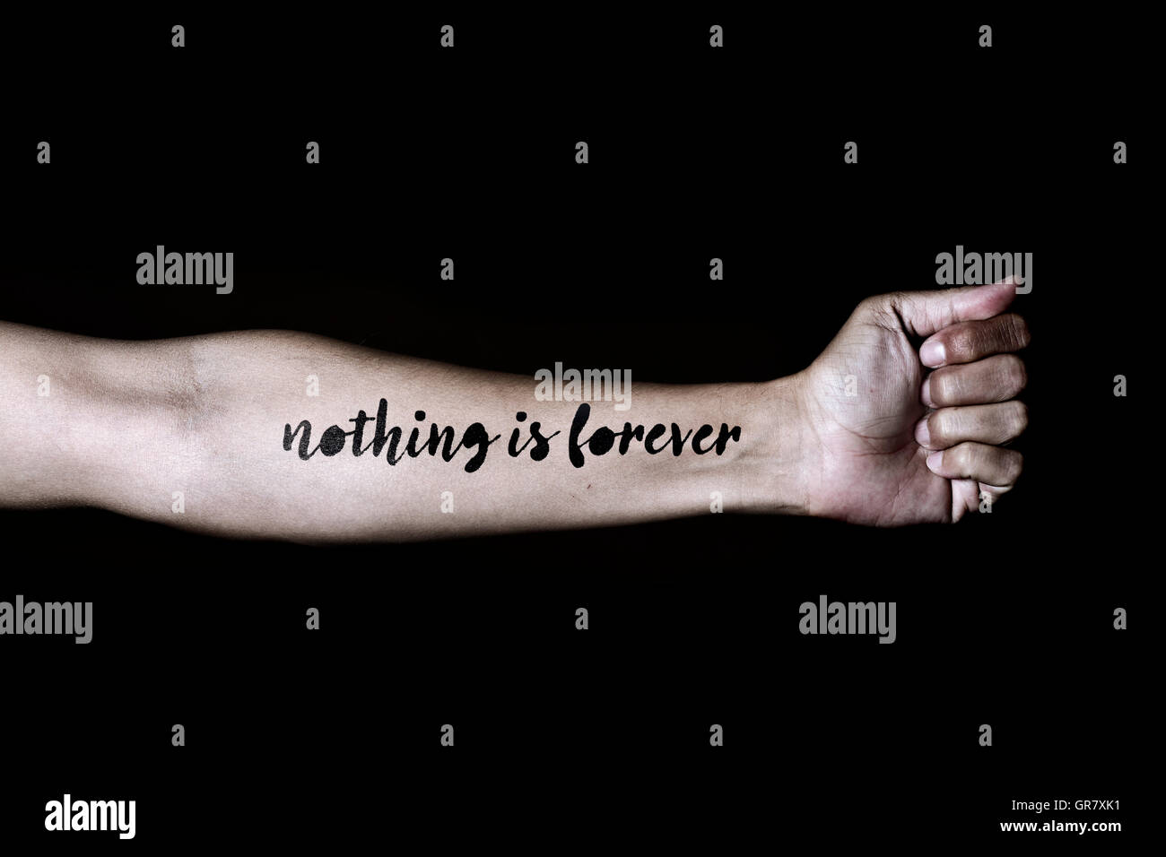 closeup of a young caucasian man with the text nothing is forever simulating a tattoo in his forearm, against a black background Stock Photo